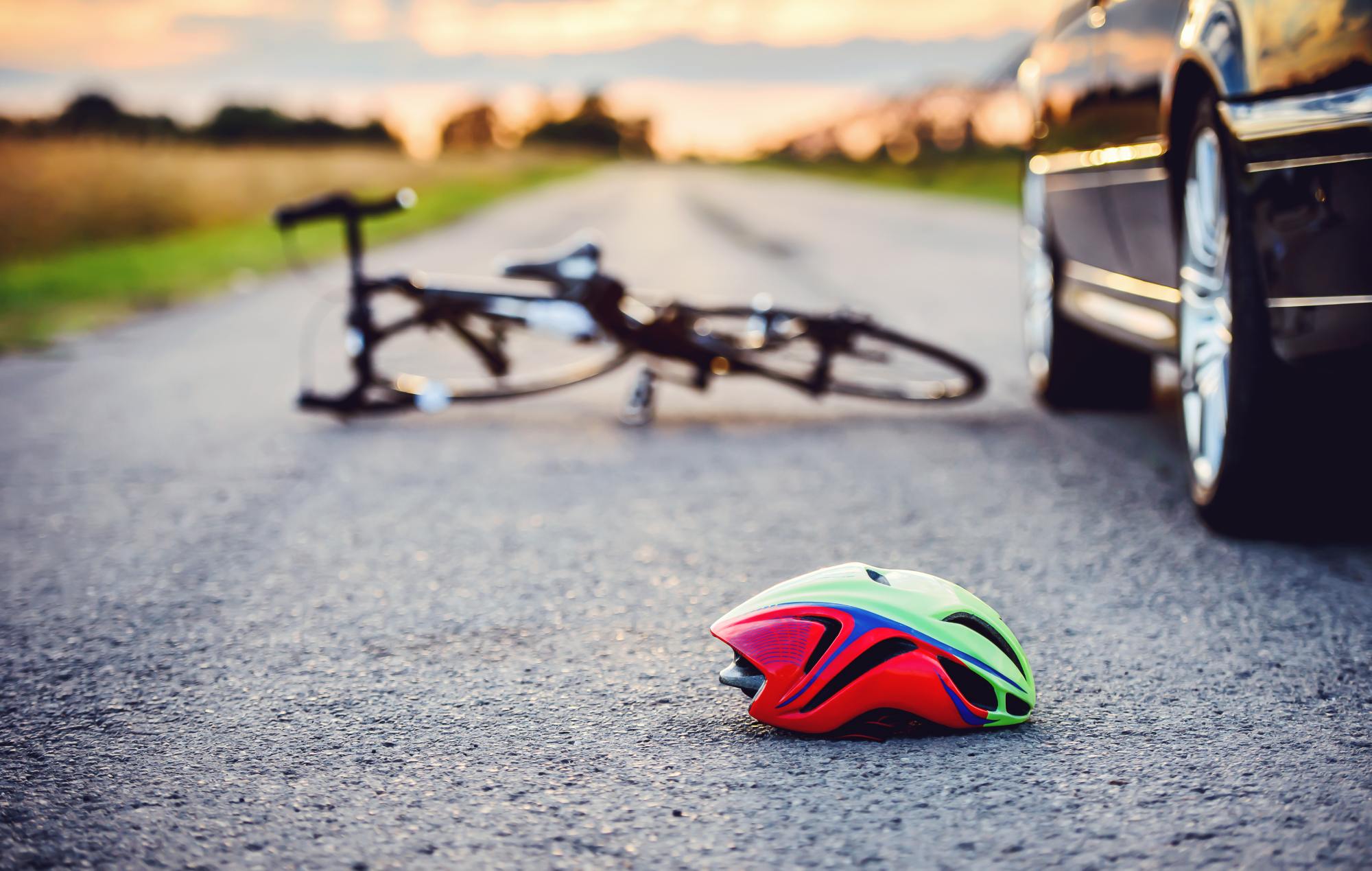 Bicicleta tirada en el suelo junto a un casco de bici y un coche parado