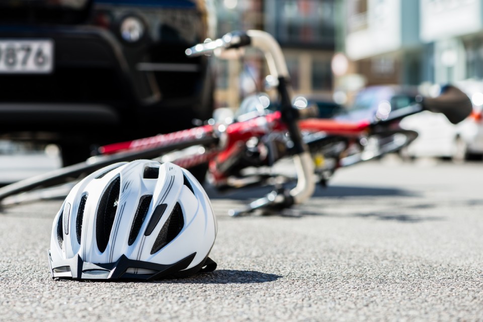 Bicicleta tirada en el suelo junto a un casco de bici y un coche parado