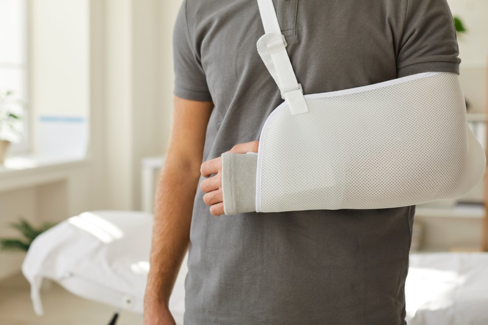 Hombre de camiseta gris con un brazo en cabestrillo